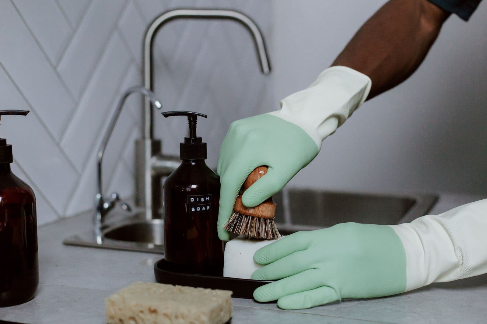 Cleaner in mint gloves scrubbing a kitchen sink with a brush