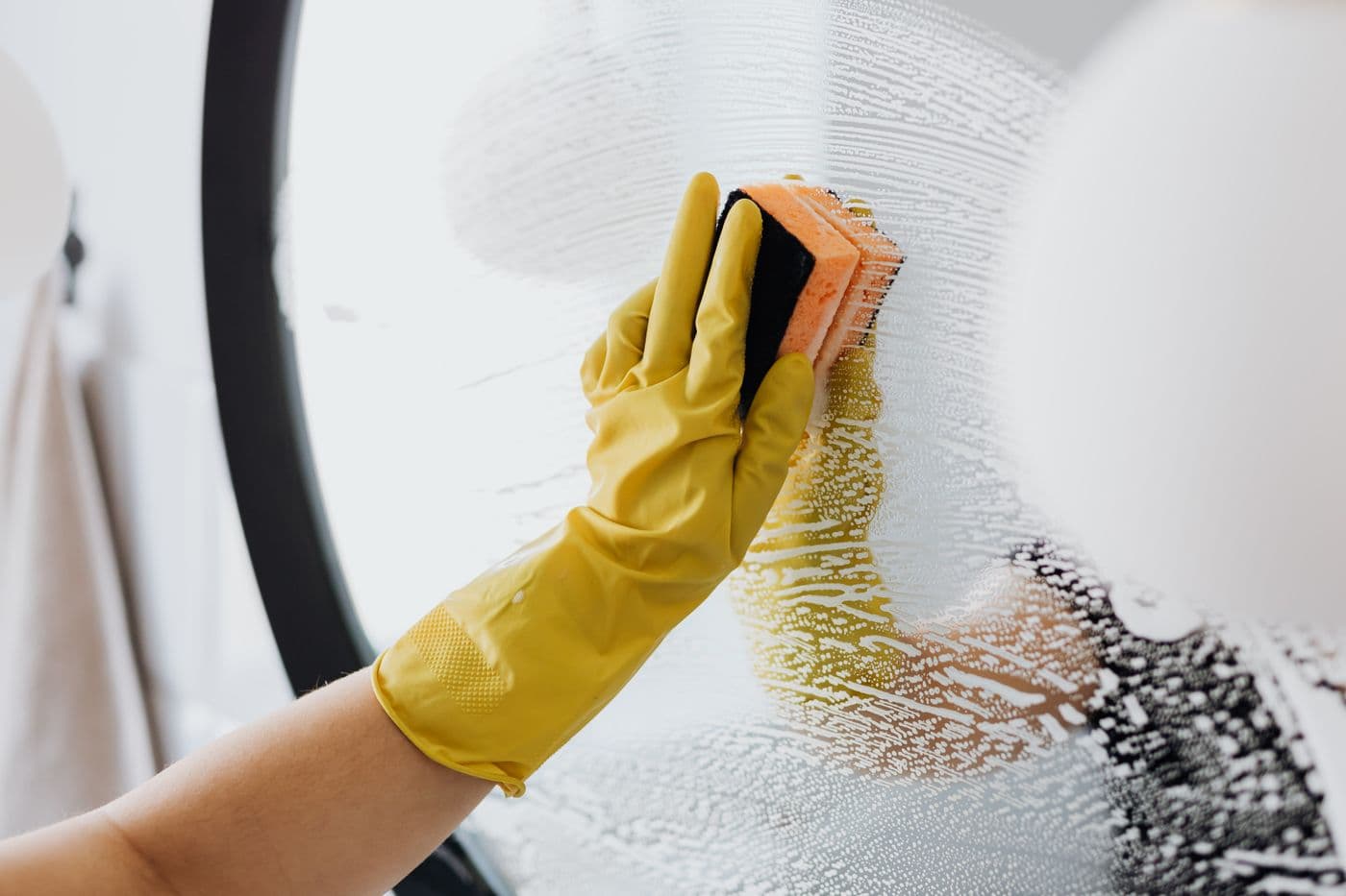 Gloved hand polishing a round mirror with a sponge